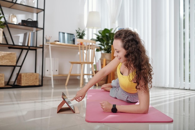 Smiling young woman following video on tablet computer when exercising on yoga mat at home