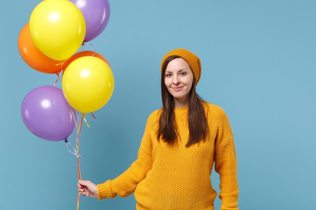 Smiling young woman girl in sweater hat posing isolated on blue background studio portrait. Birthday holiday party, people emotions concept. Mock up copy space. Celebrating hold colorful air balloons.