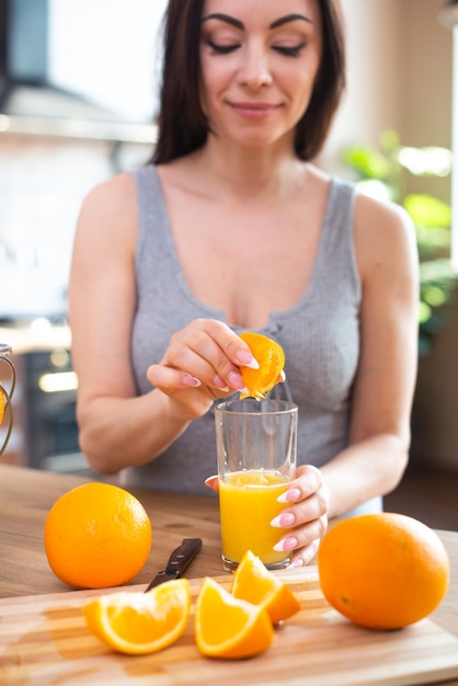 Sorridente giovane donna in una maglietta grigia spreme un'arancia fresca sul succo di frutta concetto di alimentazione sana all'interno della cucina