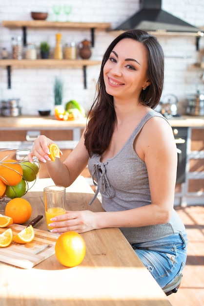 Smiling young woman in a gray Tshirt squeezes a fresh orange on fruit juice 