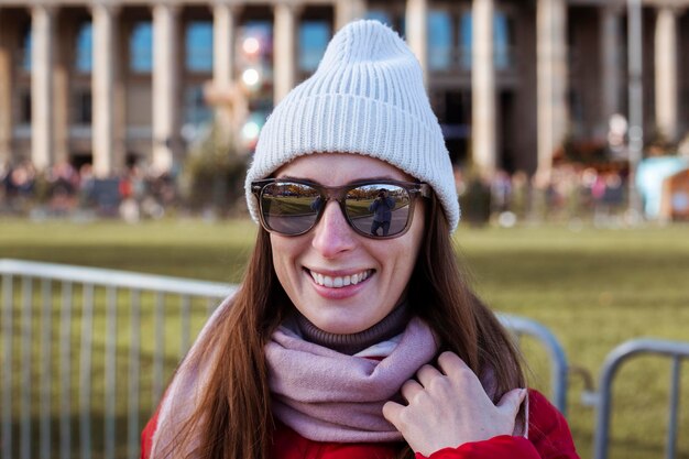 Улыбающаяся молодая женщина в шляпе с очками на улице