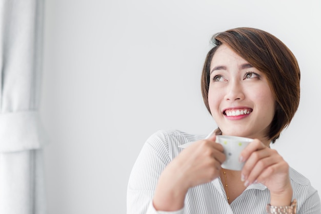 写真 笑顔の若い女性が自宅の壁にコーヒーを飲んでいる