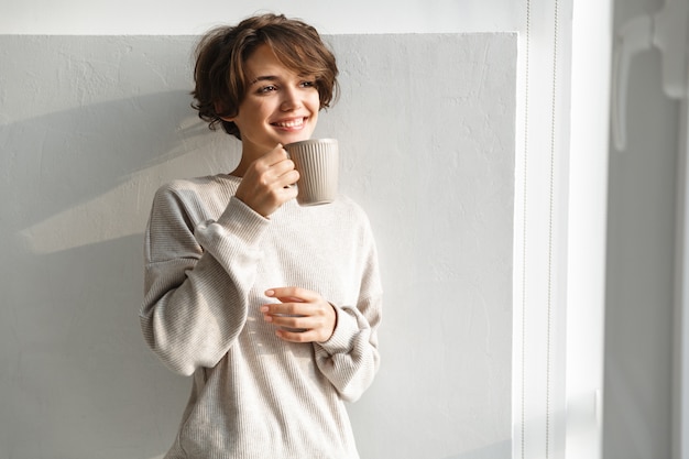 Улыбающаяся молодая женщина с чашкой чая на кухне утром