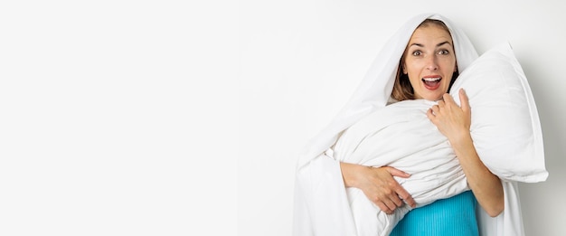 Giovane donna sorridente che si nasconde in un foglio che abbraccia un cuscino su sfondo bianco banner