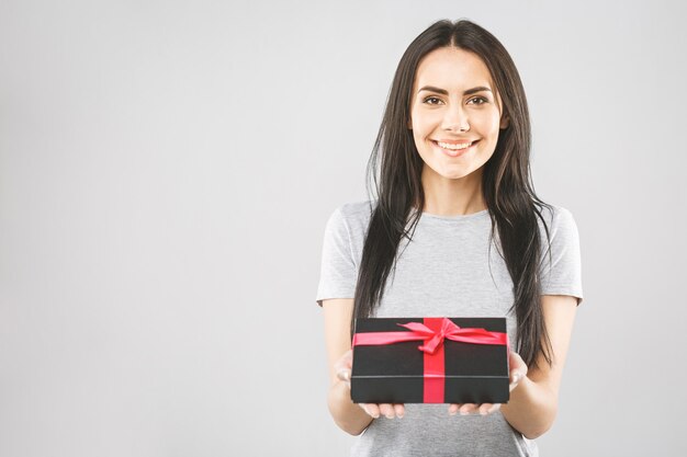 Smiling Young woman holding black gift box. Isolated over white background.