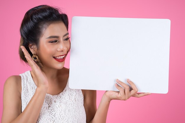 Smiling young woman holding blank placard against pink background