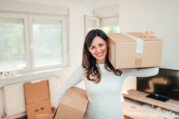 Smiling young woman holding carton boxes, looking at camera.