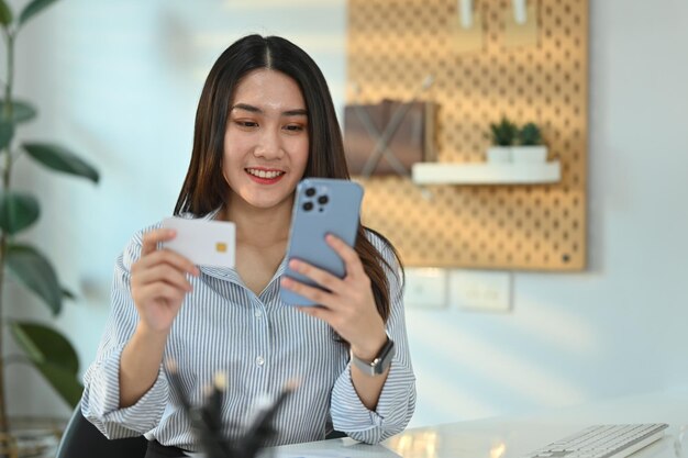신용 카드와 스마트폰을 들고 웃는 젊은 여성이 온라인으로 온라인 쇼핑 정보 입력