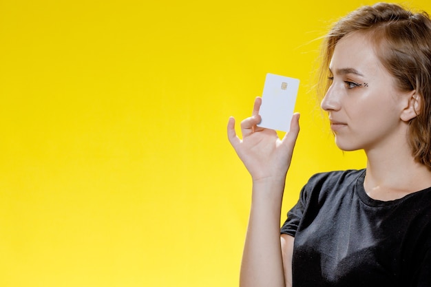 Smiling young woman holding credit card on yellow background.