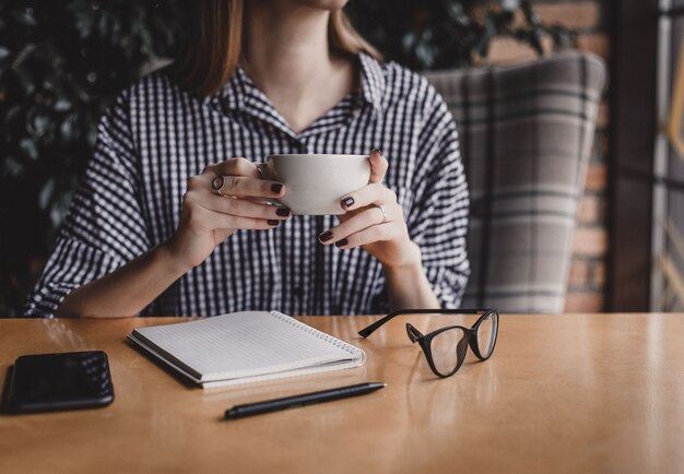 カフェでコーヒーカップとテーブルに座って眼鏡を保持している若い女性を笑顔