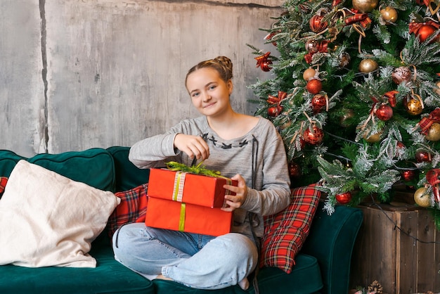 Smiling young woman holding gift box on background christmas tree at home new