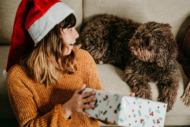 Smiling young woman holding gift sitting by sofa at home