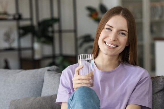 Foto sorridente giovane donna in possesso di un bicchiere di acqua pulita guardando la telecamera e sorridente. concetto di stile di vita sano