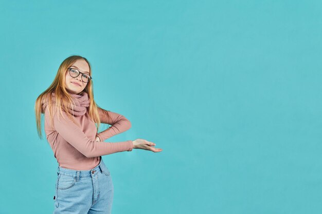 Smiling young woman holding glasses and looking at camera isolated on a blue background