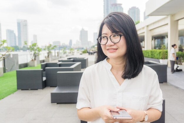 Smiling young woman holding mobile phone in city