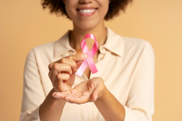 smiling young woman holding pink ribbon for breast cancer awareness