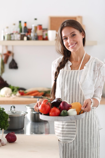 Smiling young woman holding vegetables standing in kitchen