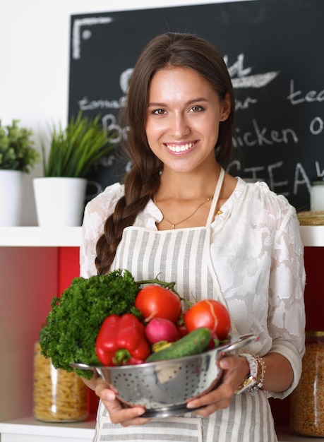 Улыбающаяся молодая женщина, держащая овощи, стоя на кухне