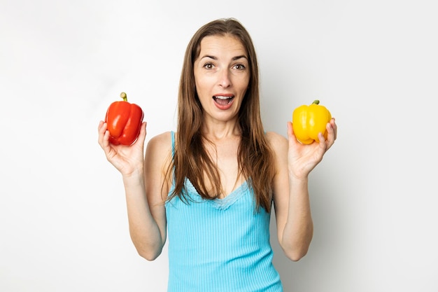 Smiling young woman holding yellow and red paprika on white background