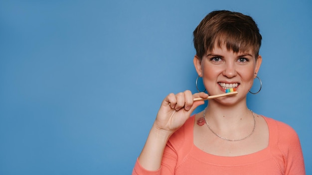 笑顔の若い女性は、青い背景で隔離の天然竹の歯ブラシを持っています。口腔衛生の概念。あなたのテキストのための場所。