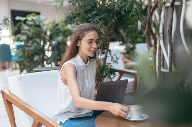 La giovane donna sorridente sta bevendo il caffè in un caffè accogliente