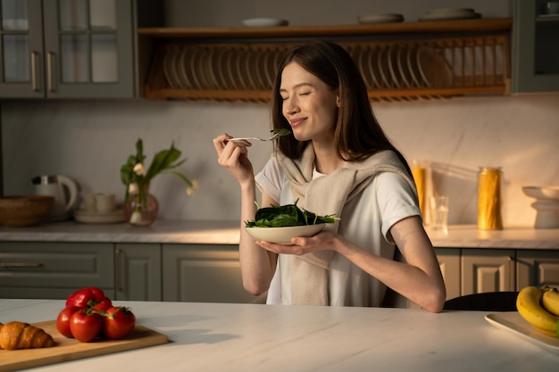 Photo a smiling young woman is sitting at a kitchen counter bathed in morning light about to enjoy a bowl