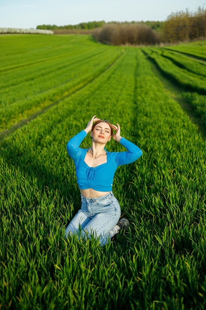 A smiling young woman is sitting in a spacious field on green grass