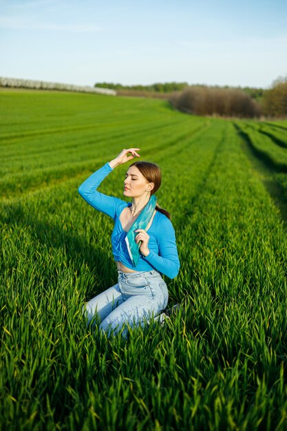 A smiling young woman is sitting in a spacious field on green grass