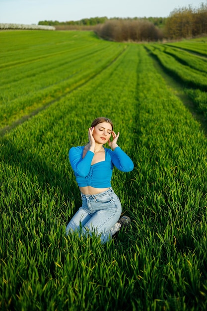 A smiling young woman is sitting in a spacious field on green grass