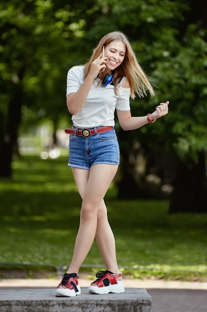 웃는 젊은 여자는 공공 공원에서 휴대 전화를 사용하고 있습니다.