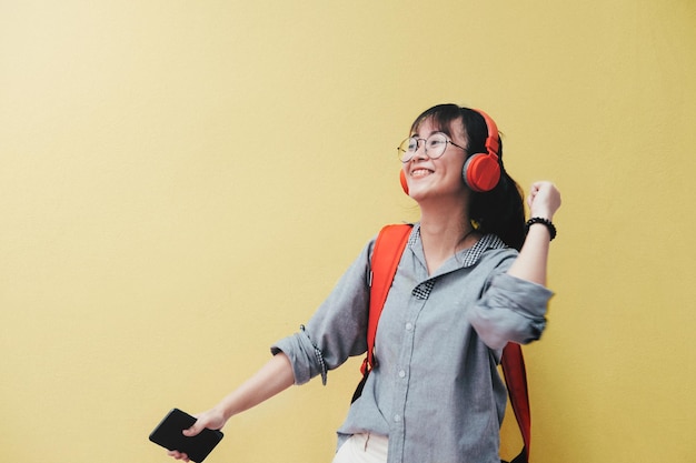 笑顔の若い女性が黄色い壁の向こうにヘッドホンで音楽を聴いています