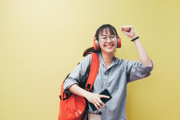 笑顔の若い女性が黄色い壁の向こうにヘッドホンで音楽を聴いています