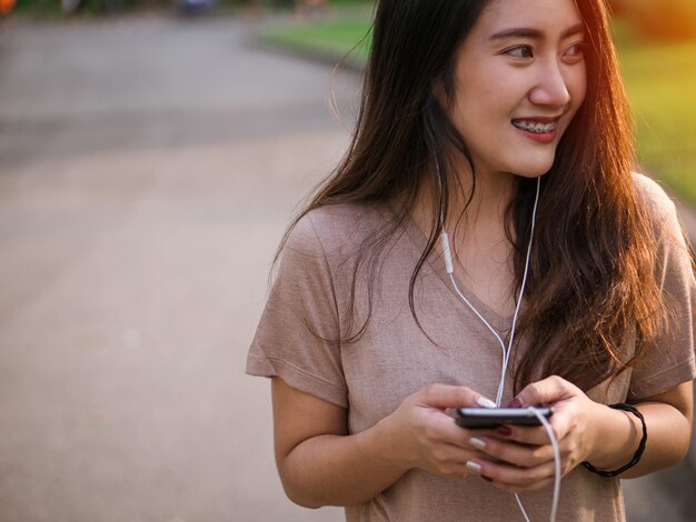 Photo smiling young woman listening to music using phone on footpath