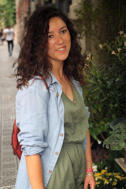 Smiling young woman looking away while standing by plants on footpath