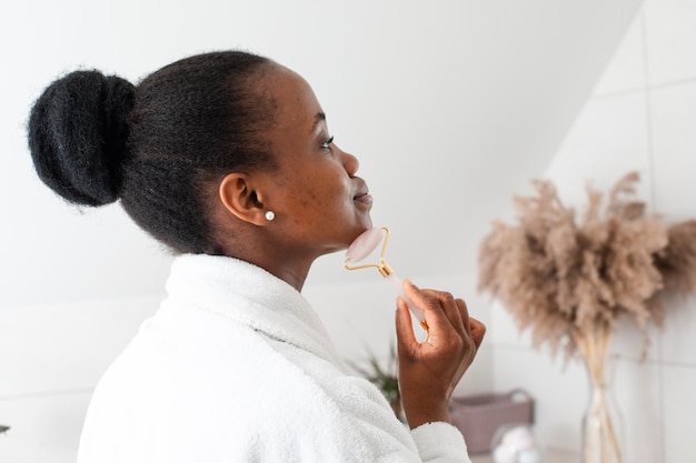 smiling young woman looking at camera massaging skin by roller