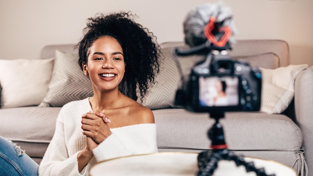 Foto giovane donna sorridente che guarda la telecamera sul treppiede nel soggiorno