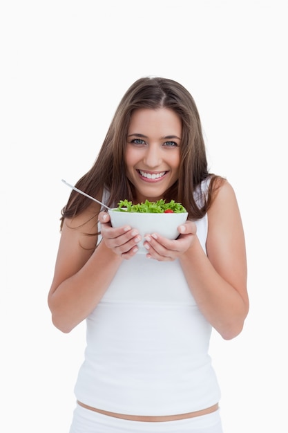 Smiling young woman looking at the camera while holding a bowl of salad