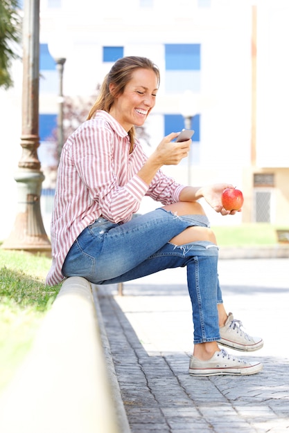 Giovane donna sorridente che esamina telefono cellulare nel parco