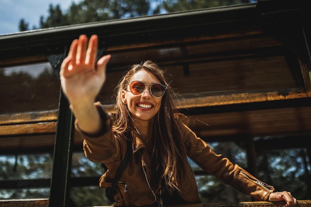 복고풍 기차로 여행하는 동안 창을 통해 손을 흔들며 바라보고 있는 웃는 젊은 여성.