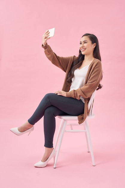 Улыбающаяся молодая женщина делает селфи на смартфоне на розовом фоне