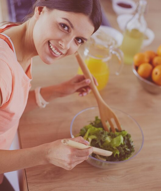 Smiling young woman mixing fresh salad in the kitchen