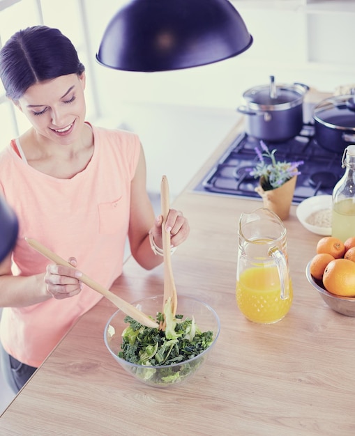 Smiling young woman mixing fresh salad in the kitchen