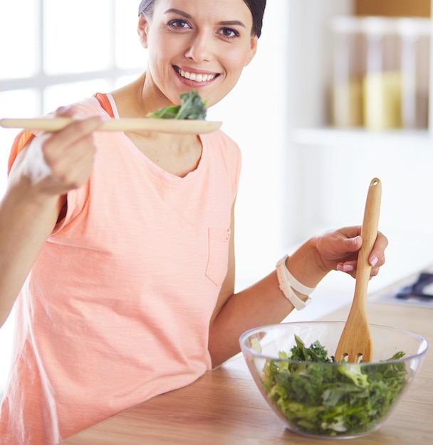 Улыбающаяся молодая женщина смешивает свежий салат на кухне