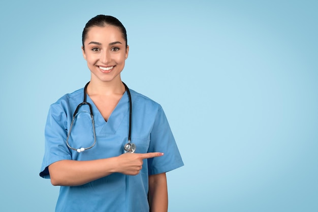 Smiling young woman nurse pointing to the side at copy space