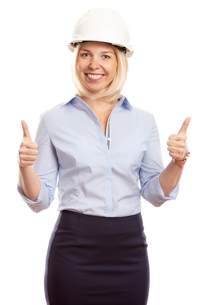 Smiling young woman in office clothes and a construction helmet on her head. Thumbs up. Vertical