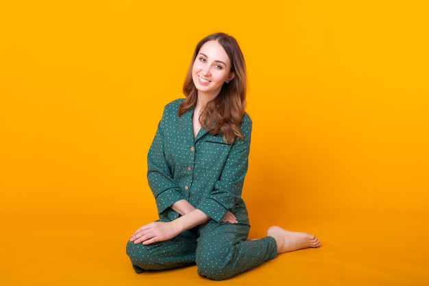 Smiling young woman in pajamas home wear posing while resting at home isolated on yellow wall