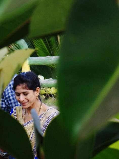 Photo smiling young woman at park seen through plants