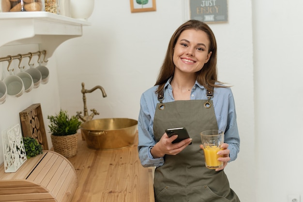 Smiling young woman on the phone standing in the kitchen, drinking juice Portrait of cheerful young.