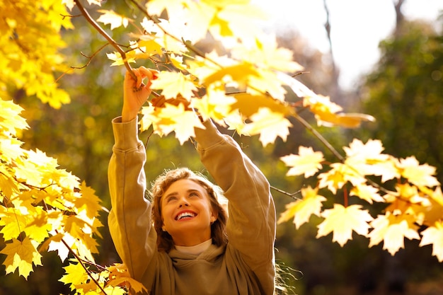 일몰 때 숲 속의 식물표본관을 위해 나뭇잎을 따고 있는 웃고 있는 젊은 여성