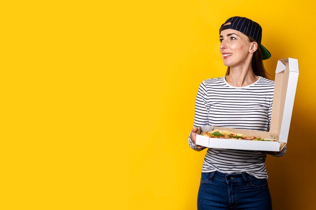 Smiling young woman pizza delivery man holding hot fresh pizza on yellow.